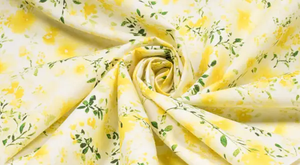 Ein zartes Popeline-Gewebe mit einem gelben Blumenmuster und grünen Blättern, das an einen sonnigen Frühlingsgarten erinnert.