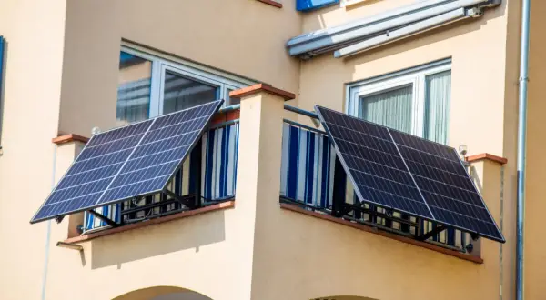 Due pannelli solari da balcone catturano l'energia del sole, montati su una ringhiera con tende a righe blu e bianche.
