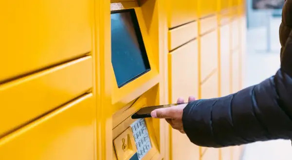 Dłoń z telefonem zbliża się do paczkomatu InPost. Dowiedz się, jak przedłużyć paczkę InPost, gdy potrzebujesz więcej czasu.