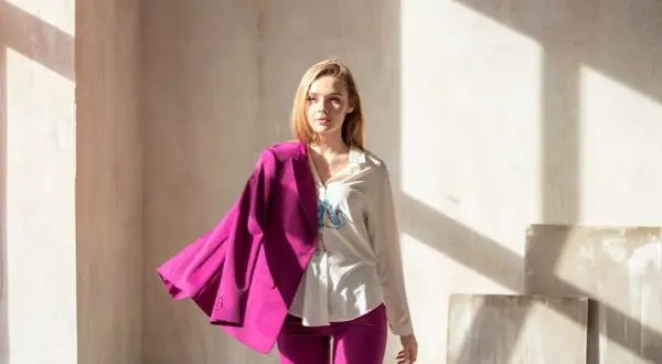 Kobieta w białej koszuli i fuksjowych spodniach, z marynarką w kolorze magenta zarzuconą na ramię. To właśnie magenta jaki to kolor!