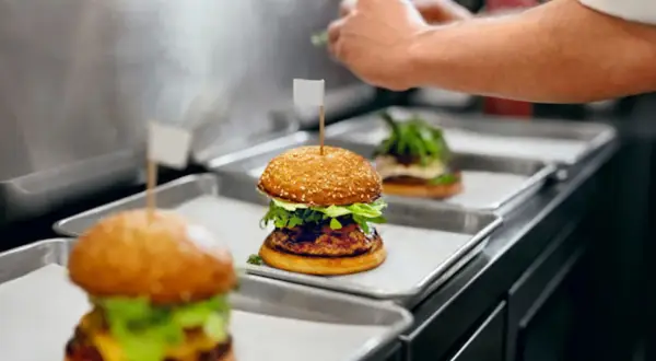 Trois hamburgers appétissants sur des plateaux, prêts pour la livraison. Une image parfaite pour une lettre de motivation restauration rapide.