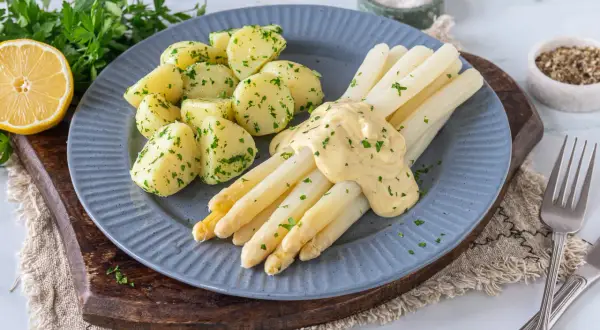 Spargel mit Sauce Hollandaise und Petersilienkartoffeln, garniert mit frischer Petersilie und einer Zitronenspalte. Ein Klassiker der deutschen Küche.