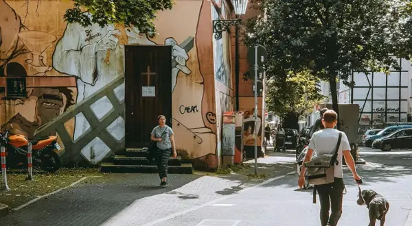 Ein Mann geht mit Hund durch eine Straße in Wuppertal, vorbei an einer Wand mit Graffiti.