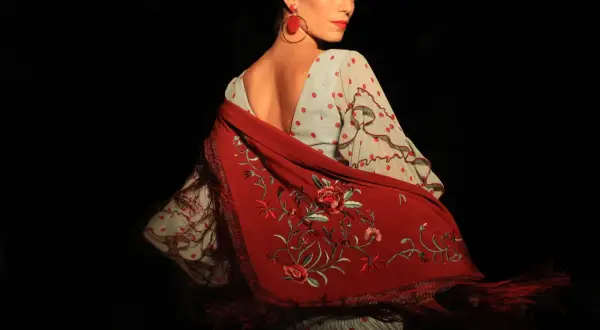 Mujer con traje de flamenca de lunares rojos y mantón bordado. Aprende como lavar un traje de flamenca para mantenerlo impecable.