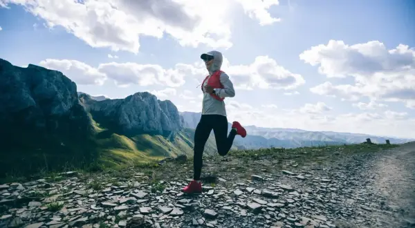 Une coureuse s'élance sur un sentier rocailleux, dominant des montagnes majestueuses. Un paysage digne d'un trail mythique en France.