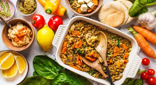 Un plat de lentilles aux légumes, une délicieuse recette végétarienne, servi avec du houmous, du pesto et des pains pita.