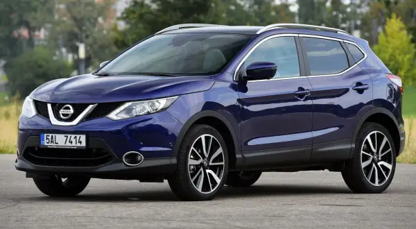 Granatowy Nissan Qashqai J11 z chromowanymi relingami dachowymi i felgami stoi na drodze.