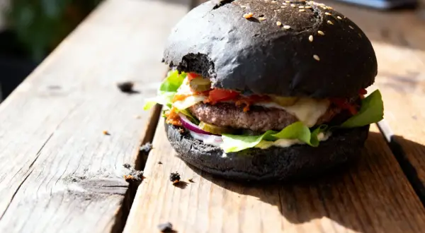 Burger maison avec pain noir, garni de salade, oignons rouges, cornichons, fromage et sauce.