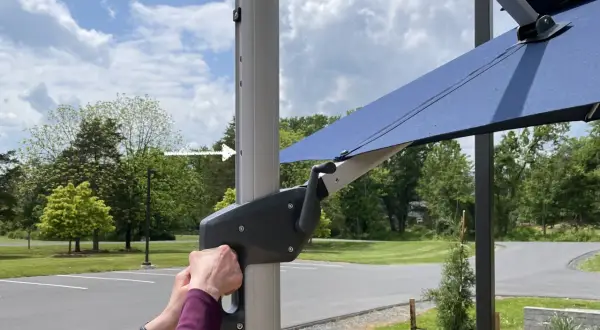 Ręce obracają korbę mechanizmu parasola ogrodowego.