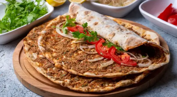 Pyszny lahmacun przepis na cienkim cieście z mięsem mielonym, pomidorami i cebulą. Obok świeża natka, cytryny i pikantne papryczki.