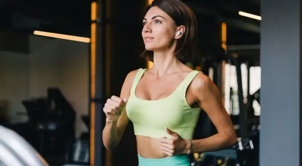 Kobieta w sportowym stroju biegnie na bieżni w siłowni.