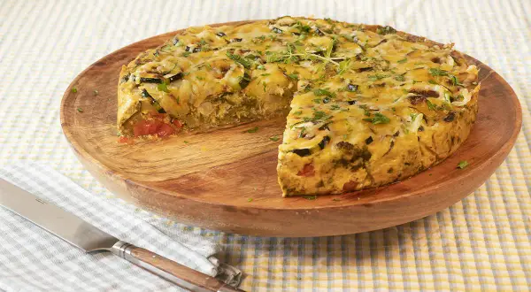 Pastel de acelgas con verduras y queso gratinado, servido en plato de madera.