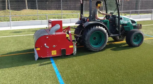 Traktor mit Anbaugerät reinigt Kunstrasen.