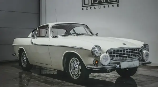Vit Volvo P1800, en ikonisk bil som påminner om James Bond. Klassisk design med kromdetaljer och runda strålkastare.