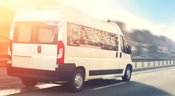 Biały bus do Niemiec pędzi autostradą w słoneczny dzień.