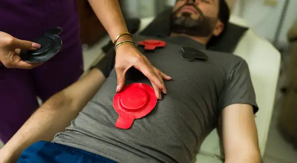 Un homme reçoit un traitement de magnétothérapie pour soulager son arthrose. Des électrodes rouges et noires sont placées sur son torse.
