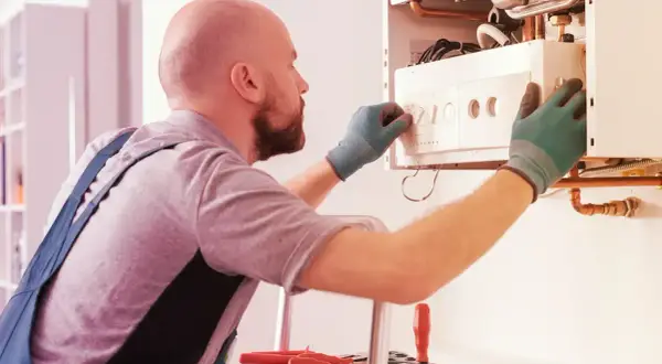 Tecnico con guanti verdi effettua la revisione caldaia in ritardo, regolando i comandi.