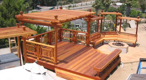 Terraza de madera de secuoya con pérgolas, bancos y hoguera. Un espacio ideal para disfrutar al aire libre.
