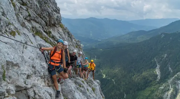 Grupa uśmiechniętych ludzi na via ferrata w Dolomitach, zabezpieczona linami, podziwia malownicze widoki górskiego krajobrazu.