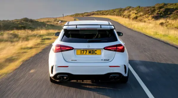Biały Mercedes-AMG A45s pędzi po krętej drodze wśród wzgórz.