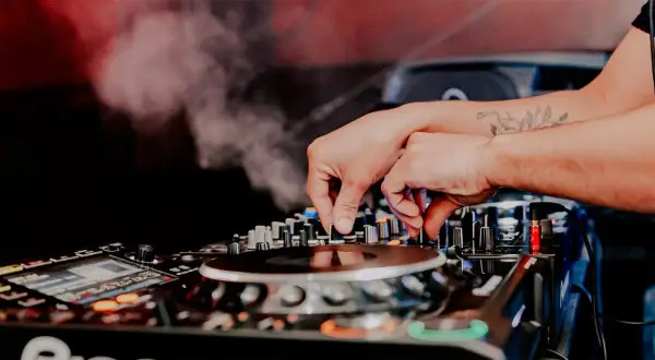 Mani esperte del dj sax mixano la musica, creando un'atmosfera vibrante con fumo e luci soffuse.