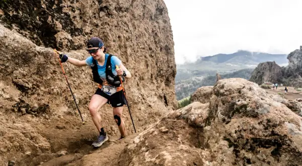 Katharina Hartmuth grimpe un sentier rocheux escarpé, bâtons en main, lors d'une course en montagne.