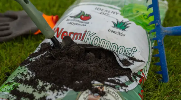 Worek z wermikompostem, łopatka i grabki na trawie. Idealny do warzywnika i trawników.