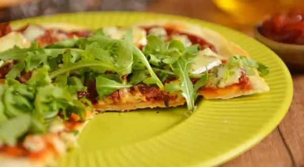 Pyszna pizza z patelni, z rukolą i serem, na żółtym talerzu.