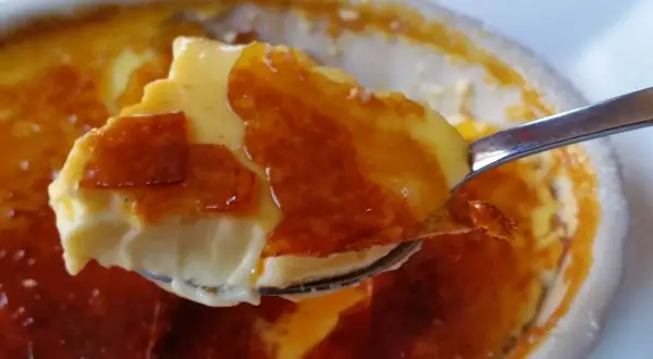 En sked lyfter en bit krämig creme brulee med knäckig yta.