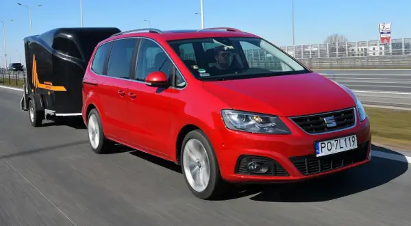 Czerwony Seat Alhambra z przyczepką na autostradzie. Kierowca w okularach. Zastanawiasz się, ile można jechać z przyczepką?