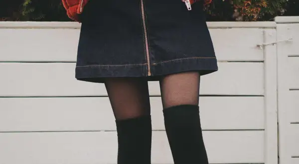 Stylowy outfit z dżinsową spódniczką, czarnymi zakolanówkami i pomarańczową kurtką.