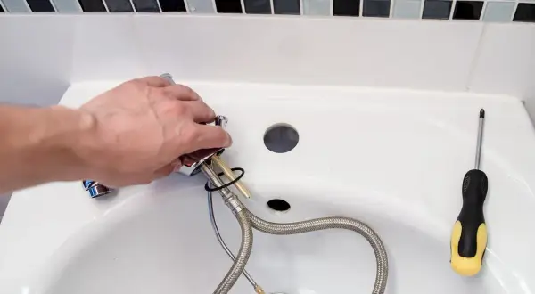 Hand montiert einen Wasserhahn, um das Waschbecken zu reparieren. Ein Schraubenzieher liegt bereit.