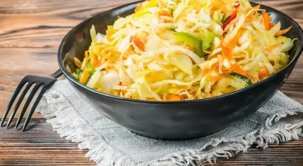 Kolorowa surówka z kiszonej kapusty inaczej, z dodatkiem marchewki, papryki i innych warzyw, podana w czarnej misce.