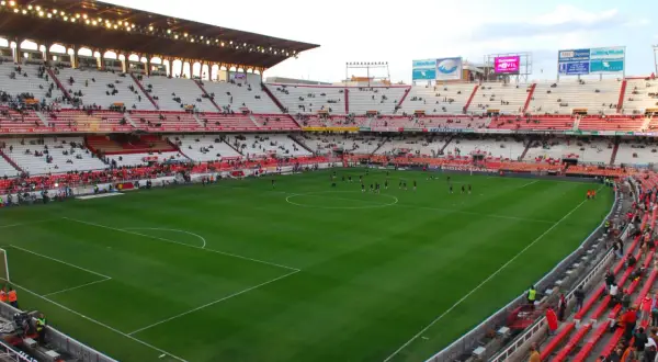 Piłkarze rozgrzewają się na murawie stadionu Sevilla. Widownia zajmuje miejsca na czerwono-białych trybunach.