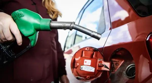 En person fyller på moms på bensin vid en röd bil. En grön bensinpump är i handen.