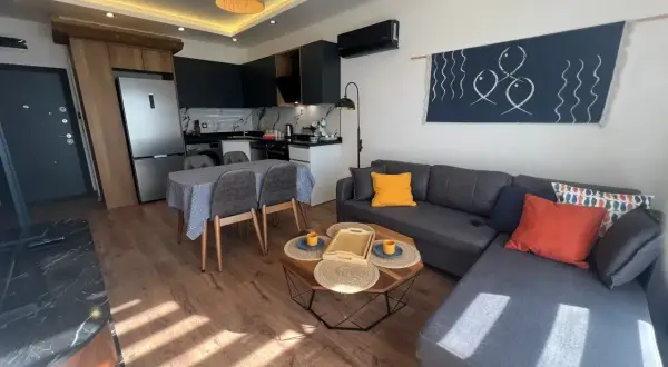 Nowoczesny salon z aneksem kuchennym, idealny na najem krótkoterminowy. Sofa, stolik kawowy, jadalnia i kuchnia.