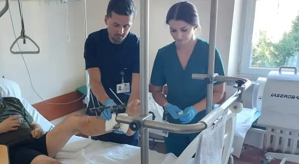 Lekarz i pielęgniarka w szpitalnej sali badają nogę pacjenta z aparatem zewnętrznym.