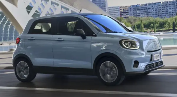 Jasnoniebieski Leapmotor T03 jedzie po drodze, z nowoczesną architekturą w tle.