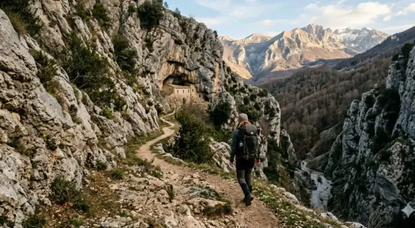 Escursionista su un sentiero roccioso, con un antico edificio incastonato nella roccia. Un viaggio che sembra un vero sentiero dello spirito tra montagne maestose.