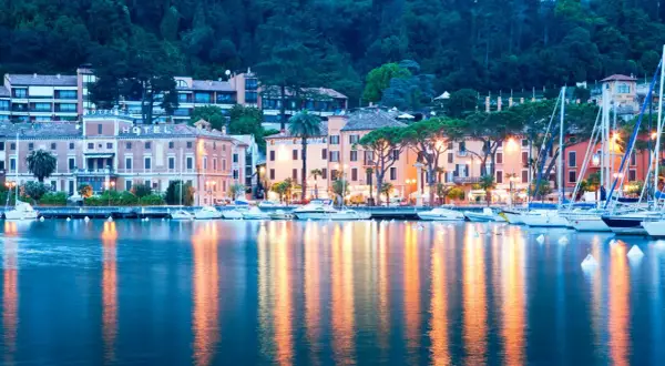 Serata a Toscolano Maderno: hotel illuminati, barche a vela e riflessi sull'acqua creano un'atmosfera magica.