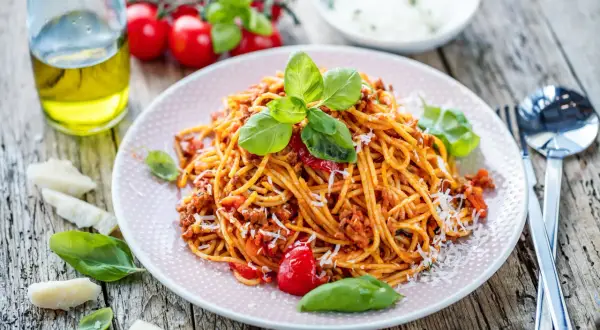 Talerz spaghetti bolognese z bazylią i parmezanem na drewnianym stole.