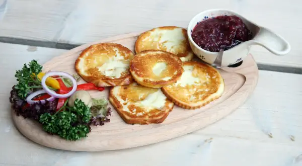 Smażony oscypek z żurawiną, podany z sałatką i pieczywem, na drewnianej desce.