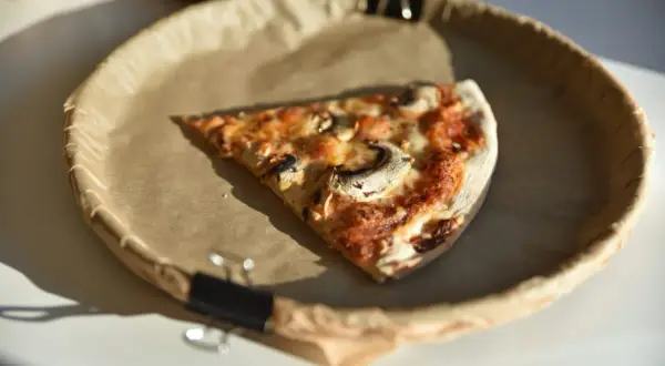 Kawałek pizzy z pieczarkami na brązowym papierze w okrągłym naczyniu.