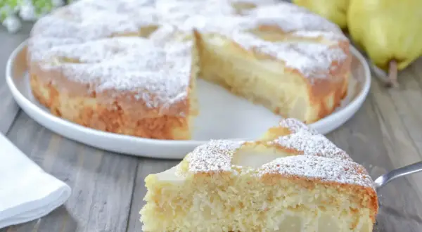 Una fetta di torta pere soffice e profumata, cosparsa di zucchero a velo, su un tavolo di legno.