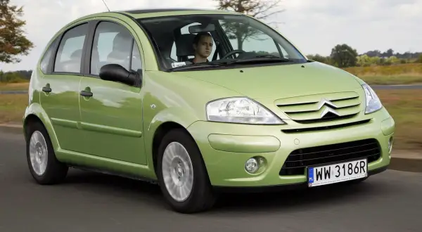 Zielony Citroen C3 z 2003 roku jedzie po drodze, za kierownicą młody mężczyzna.