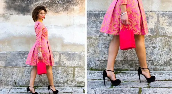 Elegancka kobieta w różowej sukience z złotym wzorem i czarnymi szpilkami. Idealne buty do różowej sukienki na specjalne okazje.