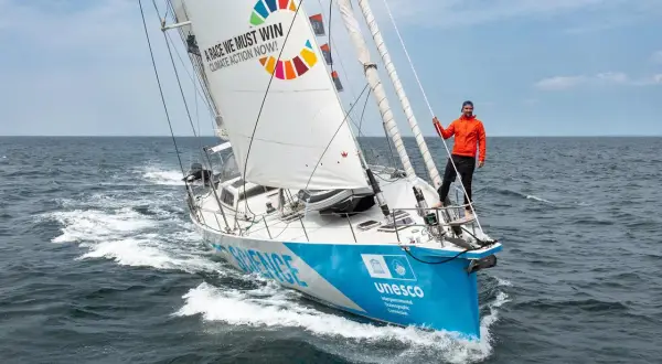 Mann auf Segelboot der Malizia Ocean Race mit Botschaft "A race we must win - Climate Action Now!".