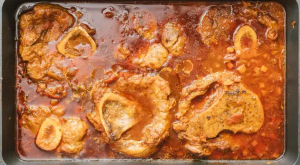 Herzhaftes Ossobuco-Rezept original italienisch: Kalbshaxenscheiben schmoren in aromatischer Sauce mit Gemüse und Kräutern in einer Bratpfanne.