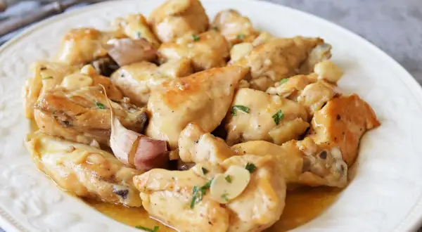 Sabroso pollo al ajillo al horno, jugoso y dorado, servido en un plato blanco con trozos de ajo y perejil picado.