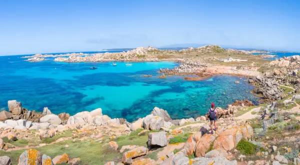 Vue panoramique de l'île Lavezzi, avec ses eaux turquoise cristallines, ses rochers granitiques et une randonneuse admirant le paysage.